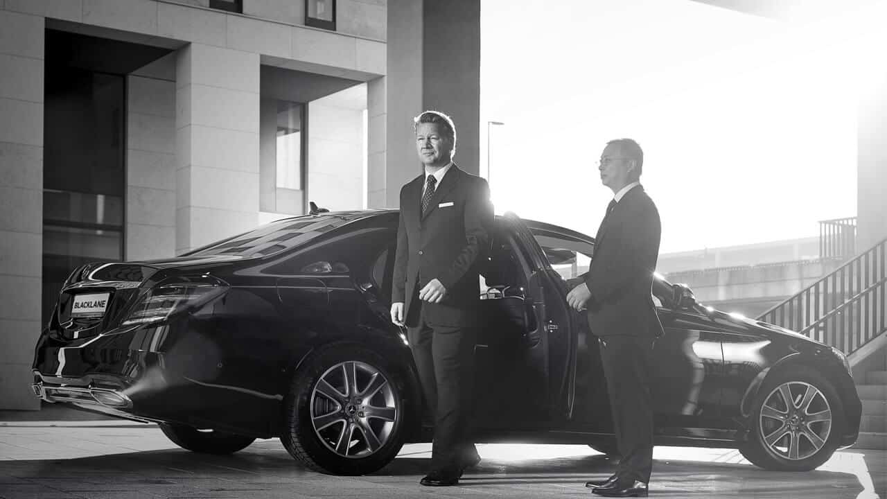 Two men in suits standing next to a car.