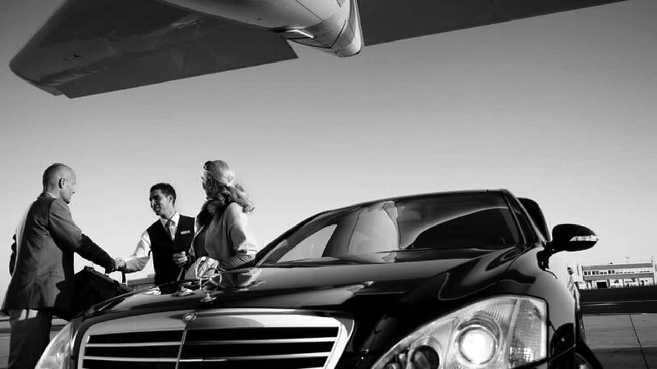 A black and white photo of a group of people standing next to a mercedes - benz.