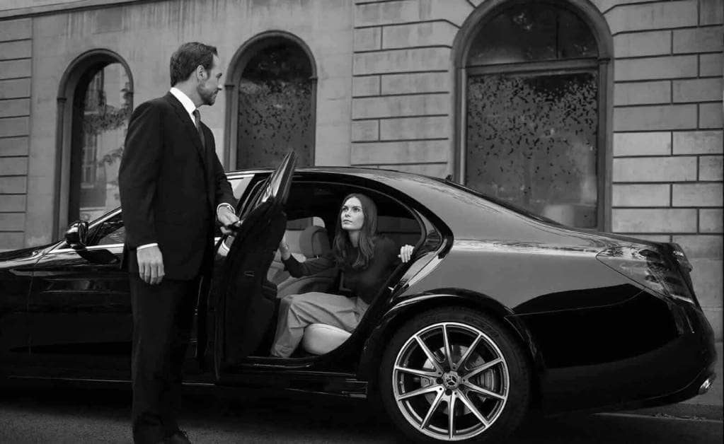 A black and white photo of a man and woman getting into a mercedes benz.