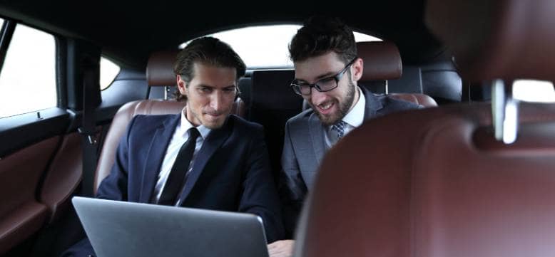 Two businessmen utilizing the best car service while examining a laptop in the back seat.
