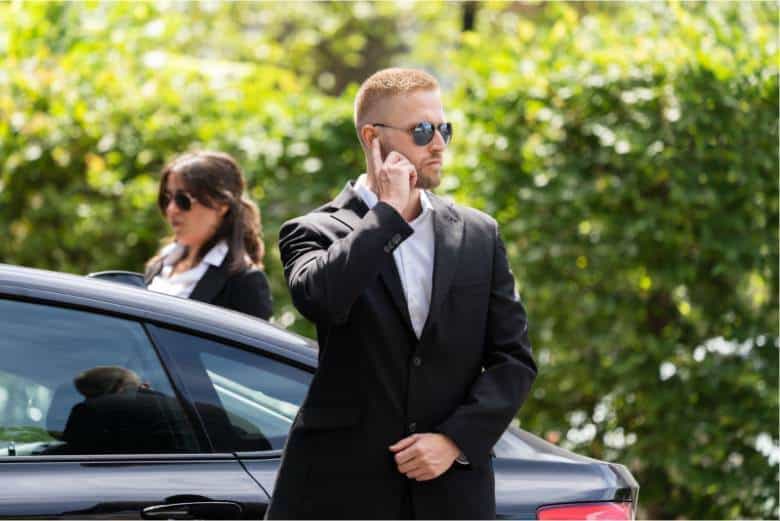 A man in a suit is standing next to a car, potentially discussing car service.